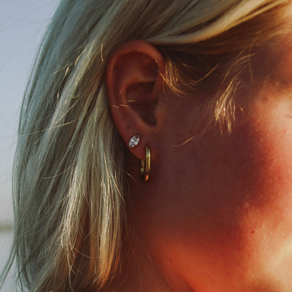 Nara Navette Earrings från Alora Avenue på modell, små eleganta örhängen med gnistrande navettslipad sten i rostfritt stål. Vattentåliga och allergivänliga örhängen som ger en tidlös och lyxig känsla till varje look.