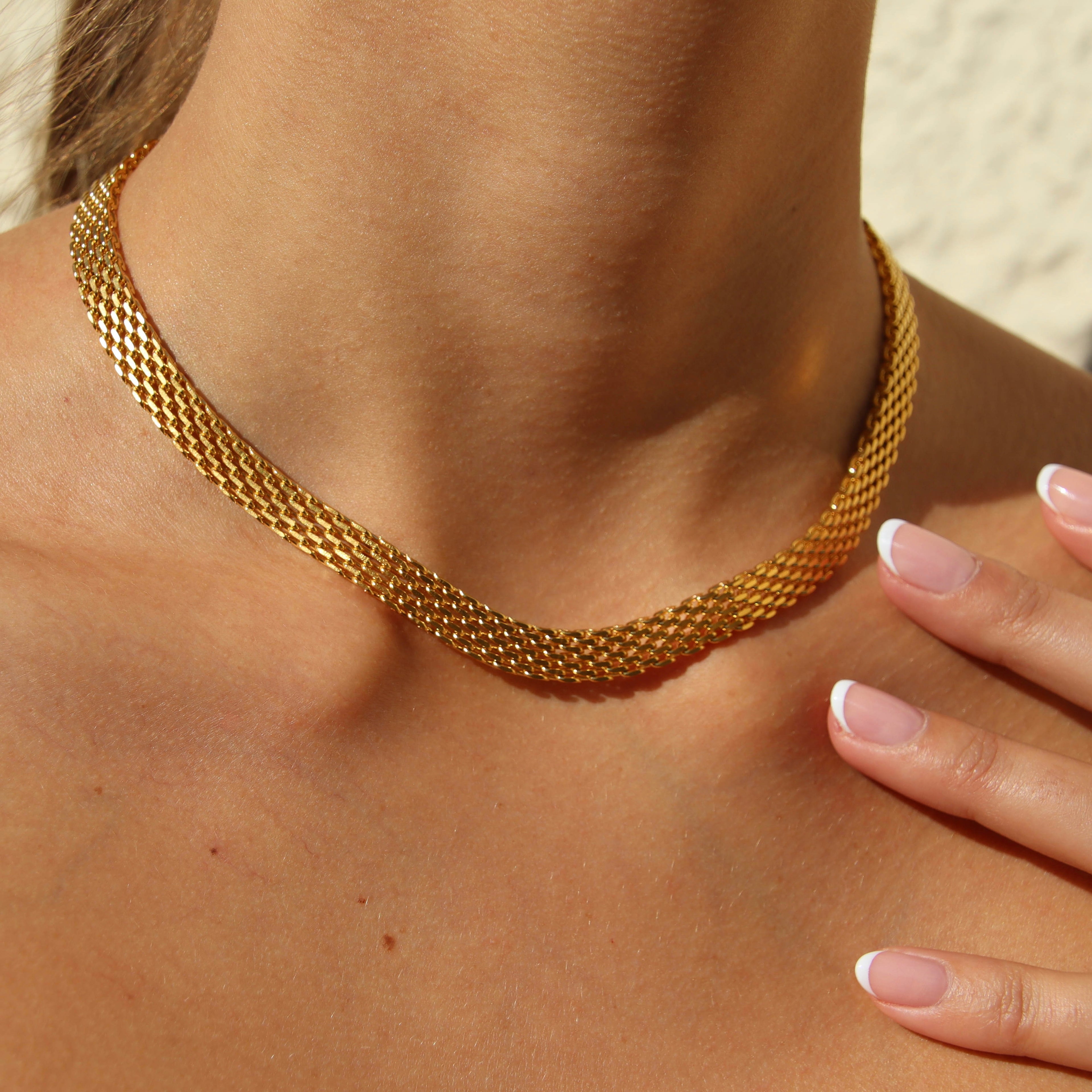 Airy Aurora Necklace i guld runt halsen, fångat i solens ljus. Ett glänsande, elegant halsband från Alora Avenue – vattentåligt och tidlöst i designen.