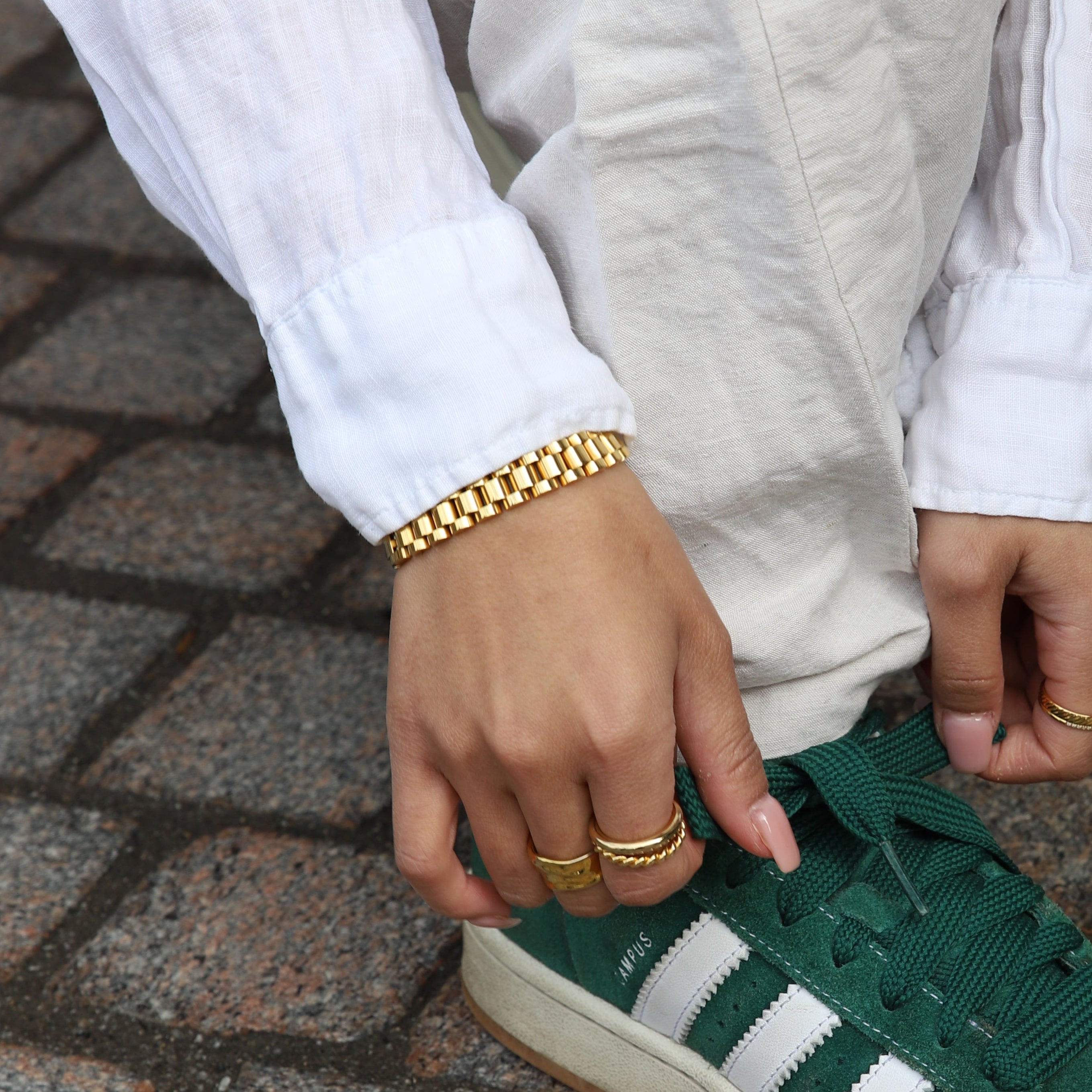 Analog Aria Wristband i guldfärgat rostfritt stål stylat med vita byxor och adidas sneakers – ett vattentåligt och allergivänligt armband med klockinspirerad design för en tidlös vardagslook.