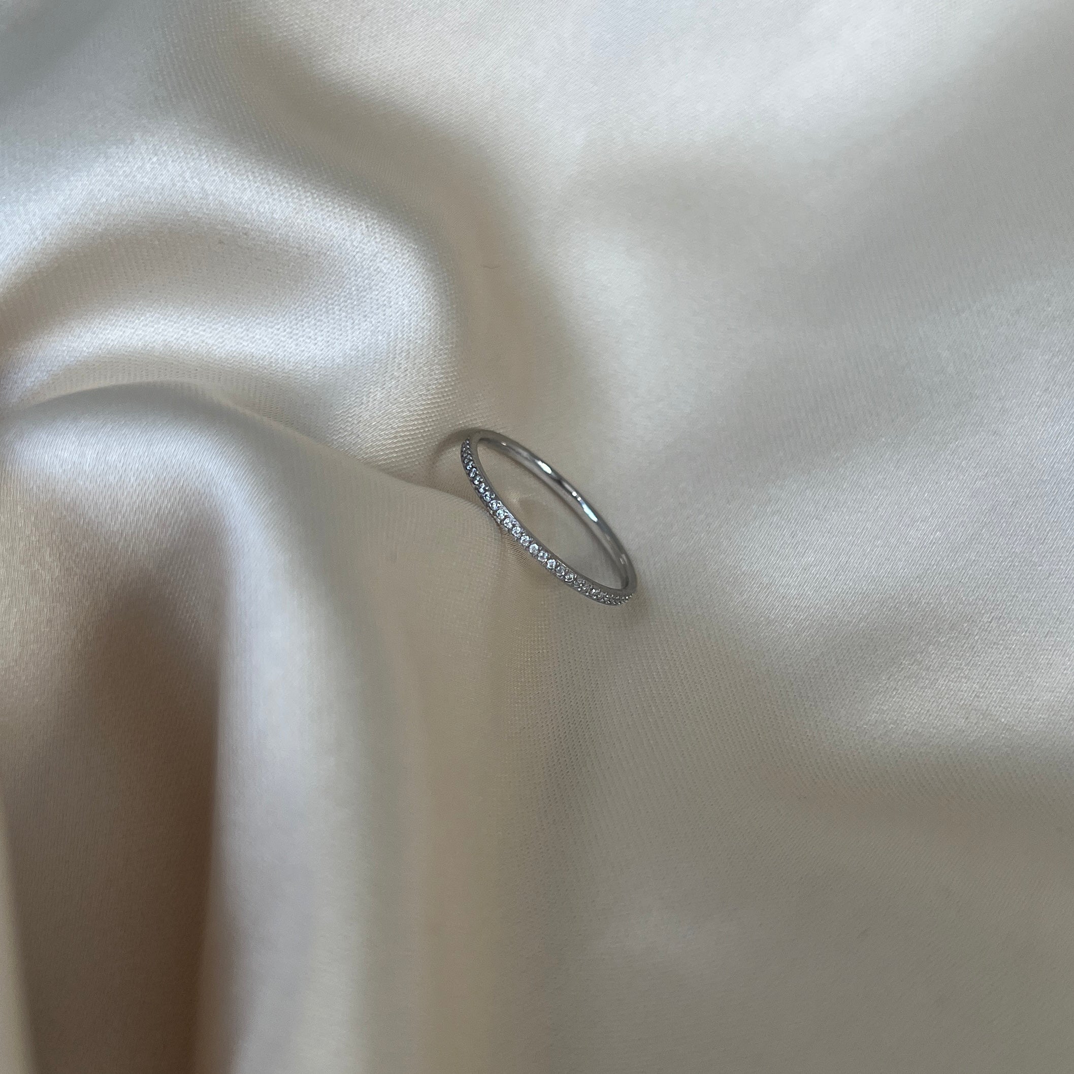 Isla Spark Ring i silver med gnistrande stenar fotograferad på ljus sidenbakgrund. Minimalistisk, vattentålig och allergivänlig ring från Alora Avenue.