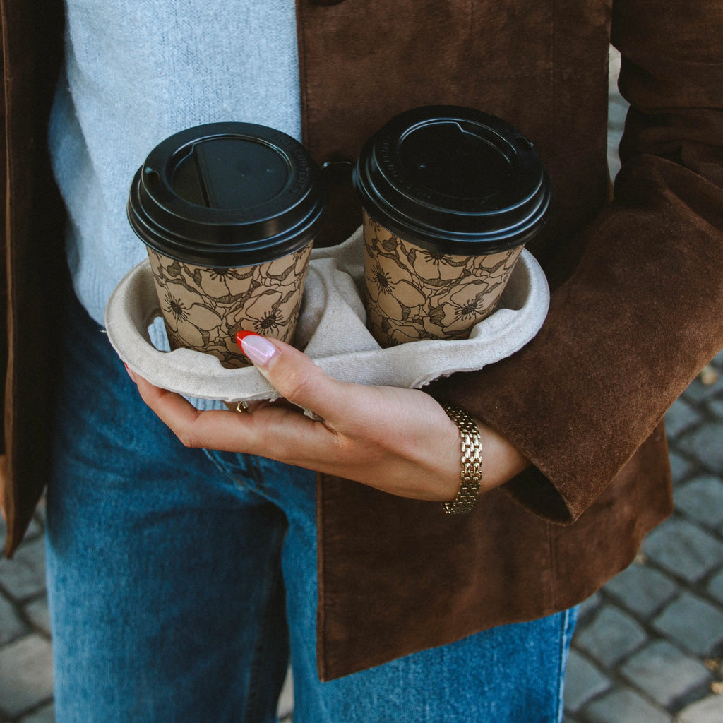 Maya Magnolia Bracelet i guld på handled, stylat med två kaffekoppar och brun mockajacka. Elegant och vattentåligt armband från Alora Avenue med tidlös design.