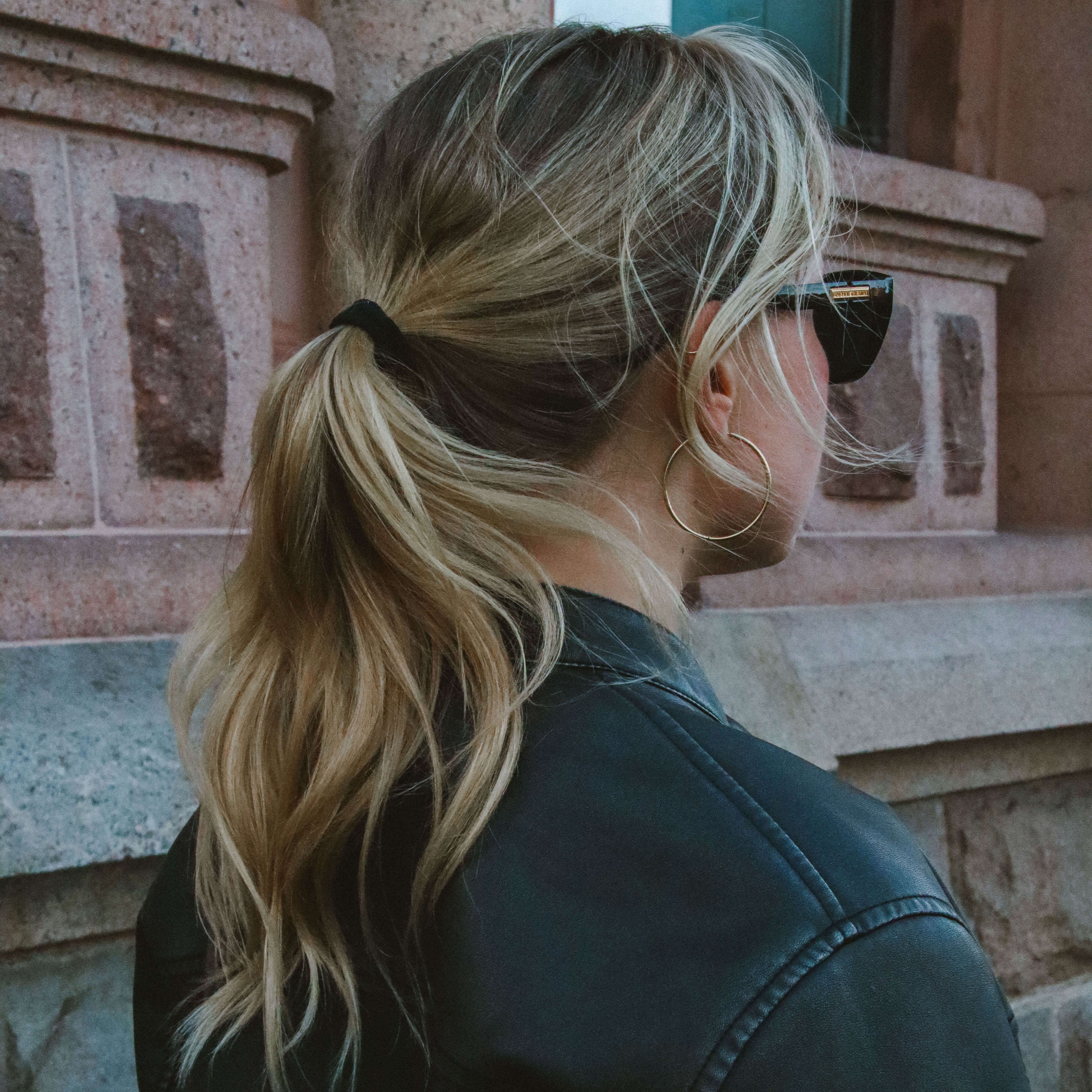 Kvinna i svart skinnjacka bär Sky Saturn Hoops i guld – stilrena, vattentåliga och allergivänliga örhängen i rostfritt stål. En elegant kontrast mellan lyxig glans och vardaglig edge, perfekt för höstens streetstyle.