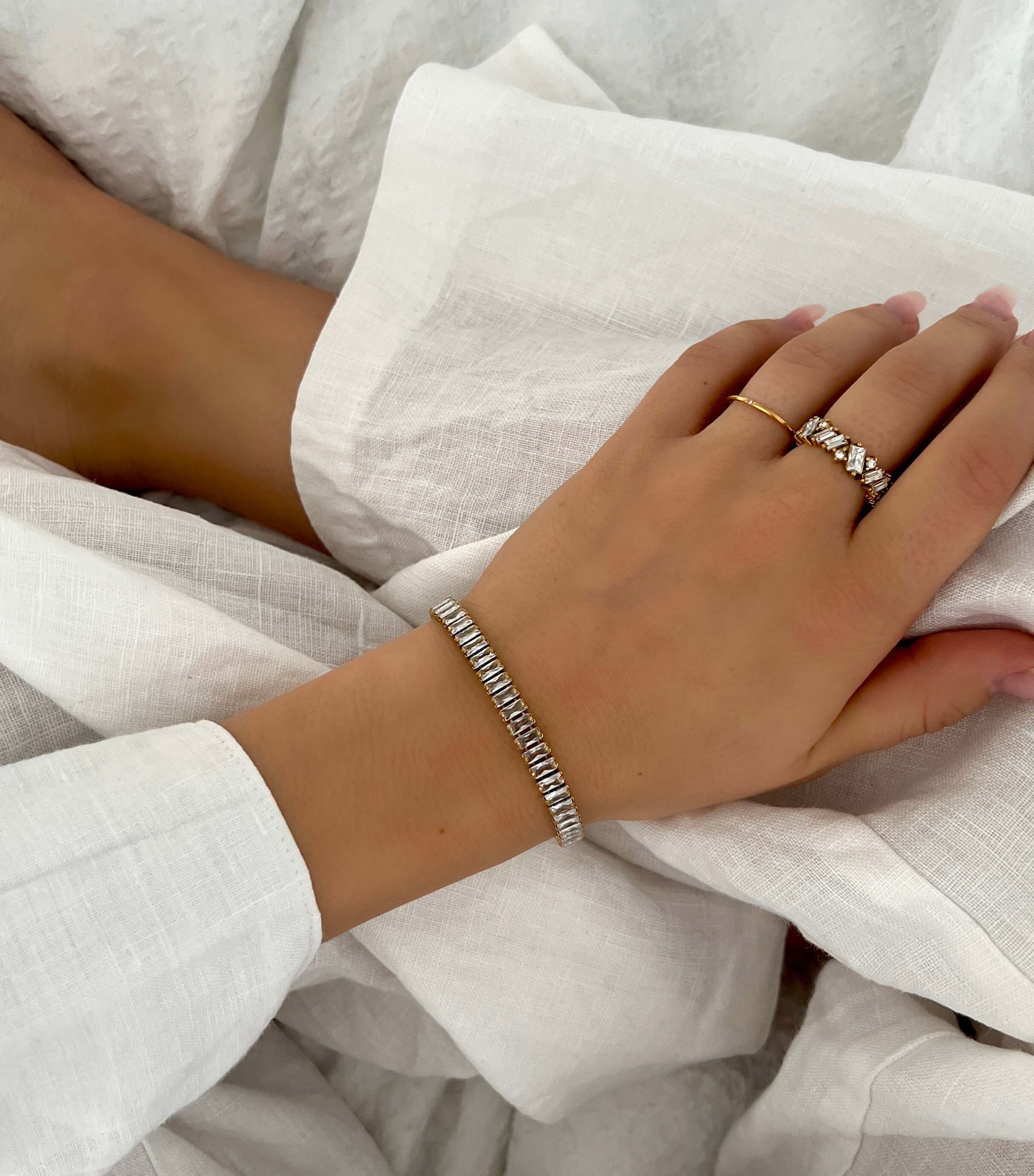 Solo Dazzle Ring stylad med fler ringar – tunn guldfärgad ring med en liten klar sten. Matchas här med en bredare kristallring och ett silverfärgat armband. Vattentålig och allergivänlig – tillverkad i rostfritt stål med slitstark PVD-plätering. Elegant för både vardag och fest.