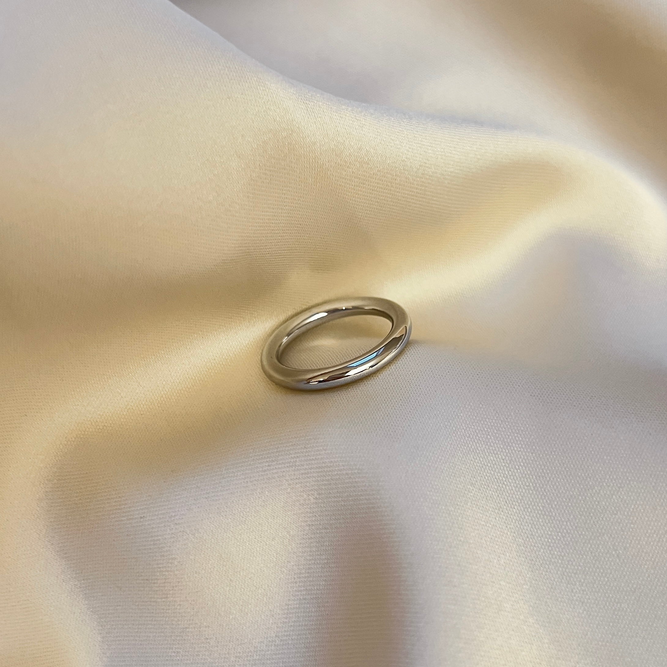 Tampa Tube Ring från Alora Avenue – en stilren och chunky silverfärgad ring i rund form, fotograferad mot mjukt skimrande tyg. En modern basring som passar till allt.